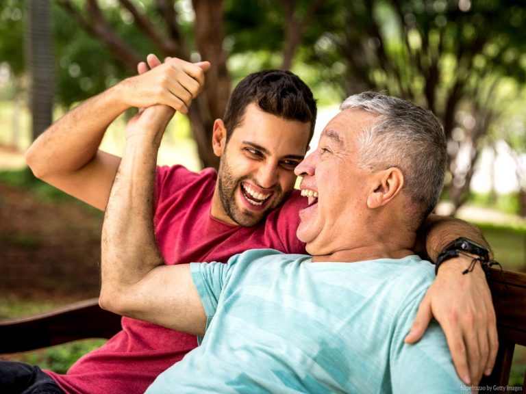A man and his elderly father smiling and holding hands after discussing a debt management plan