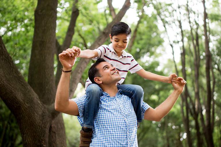 A young boy smiling as he sits on his dad's shoulders