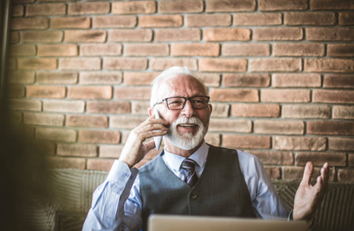 An elderly business man smiling as he talks on the phone